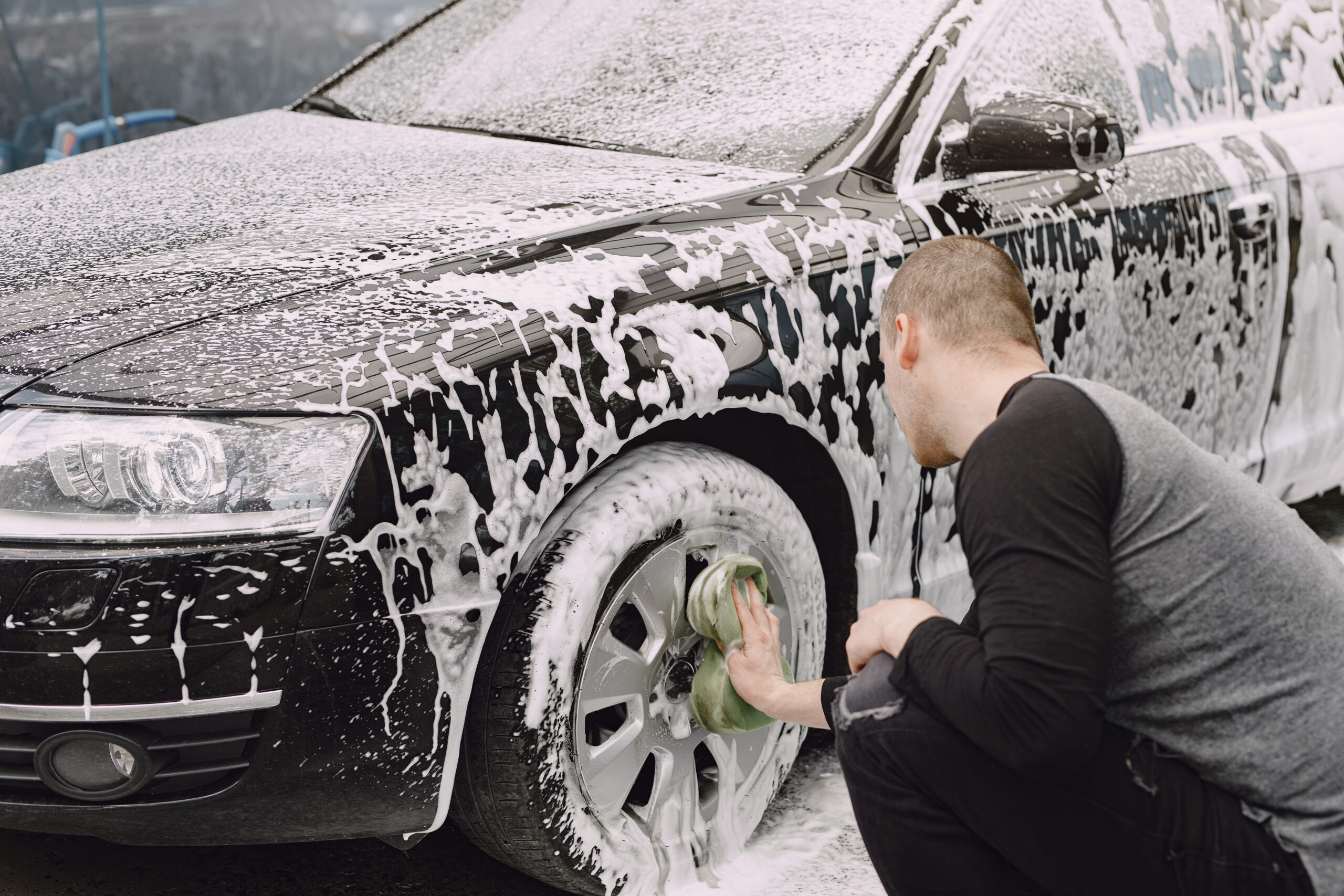 Man in a  black sweater. Male washing a car. Guy spray a water.