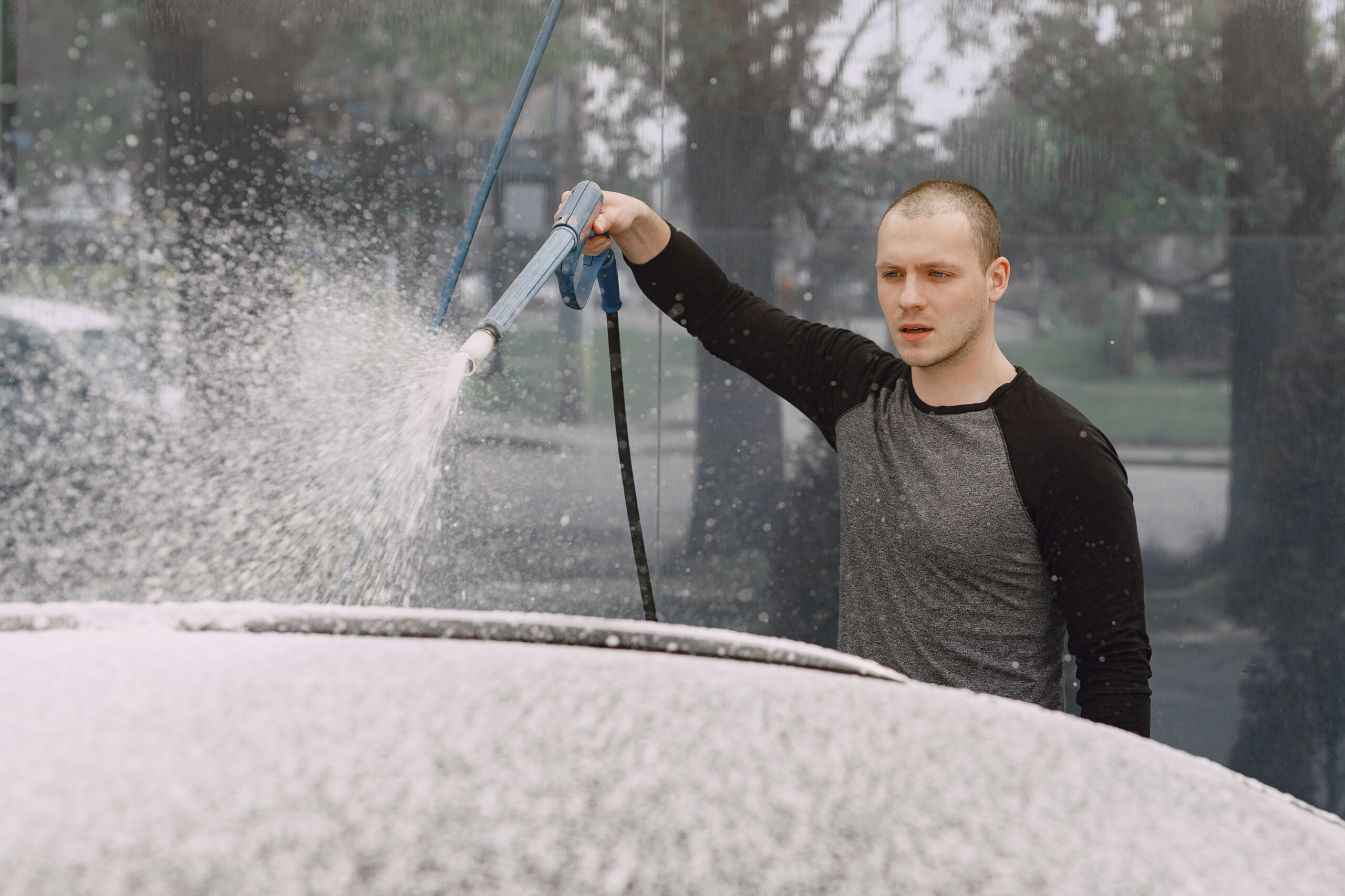 Man in a  black sweater. Male washing a car. Guy spray a water.