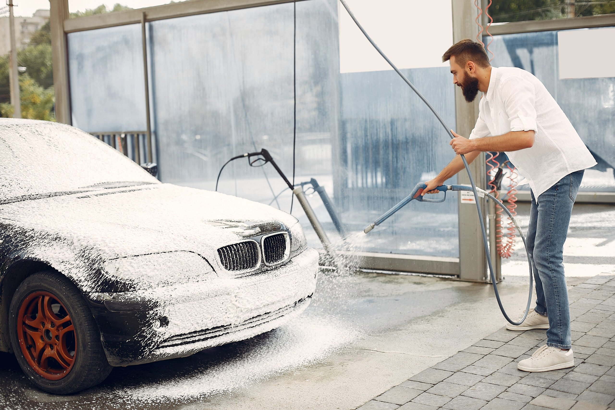 Man in a white shirt. Male washing a car. Guy spray a soap